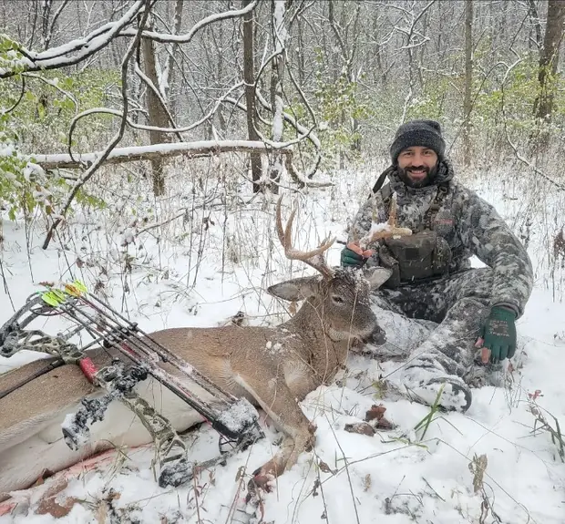 A bowhunter with a whitetail buck and compound bow in the snowy woods